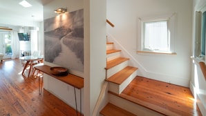 Ein modernes Interieur mit einer Holztreppe, einem Essbereich mit Tisch und Stühlen sowie einem großen abstrakten Gemälde an der Wand.