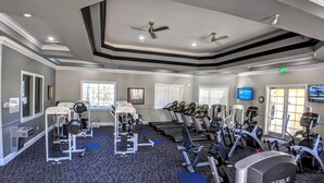 A gym with various exercise equipment, including treadmills, weight machines, and a ceiling fan. - Cosy Condo near Disney and Parks. season price. (Kissimmee)