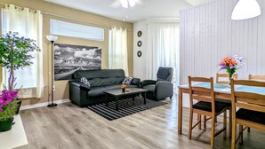 A living room with a sofa, coffee table, and dining table with chairs. There is a ceiling fan, a lamp, and a painting on the wall. - Cosy Condo near Disney and Parks. season price. (Kissimmee)