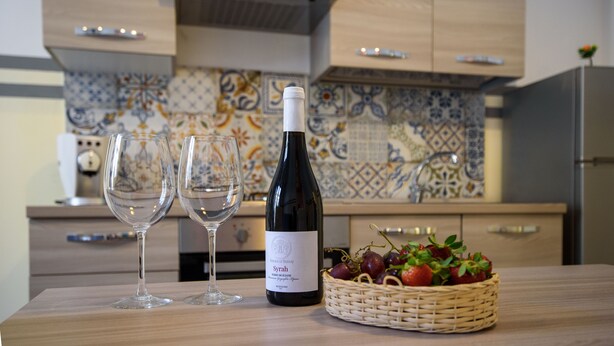 A kitchen with two wine glasses, a bottle of wine, and a basket of fruit on the counter. - Housestation (Palermo)