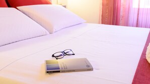 A neatly made bed with white and red pillows, a pair of glasses, and a book titled "La camera chiara" on the bed. - Housestation (Palermo)