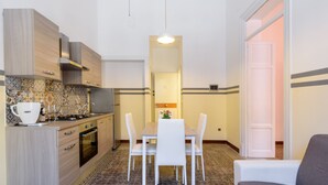 A compact kitchen with a dining area, featuring a tiled backsplash, wooden cabinets, and a central table with chairs. - Housestation (Palermo)