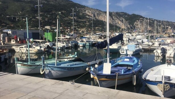 Un port de plaisance avec des bateaux amarrés, un ciel dégagé et une chaîne de montagnes en arrière-plan.