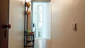 Un couloir avec un plancher en bois, un présentoir en métal où sont posés des sacs, et une porte donnant sur une salle de bain.