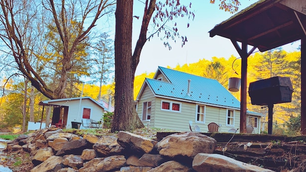 Une cabane rustique avec un toit bleu, entourée de gros rochers et d’arbres.