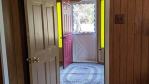 Une porte en bois, dotée d’un cadre blanc, donne sur un porche abrité où se trouve un tapis en fibres tressées.