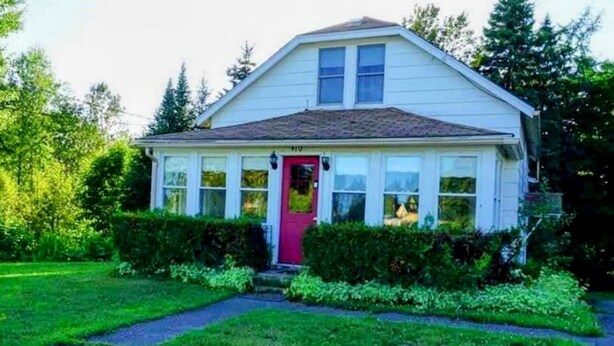 A single-story house with a red front door, white siding, and a small front porch.