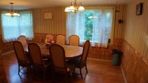 A dining room with a wooden table and chairs, a chandelier, and a window with curtains.