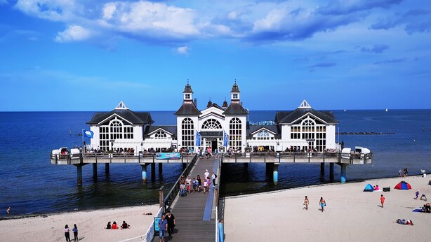 Un muelle con un edificio blanco que presenta ventanas de arco y una torre central, que se extiende sobre la playa.
