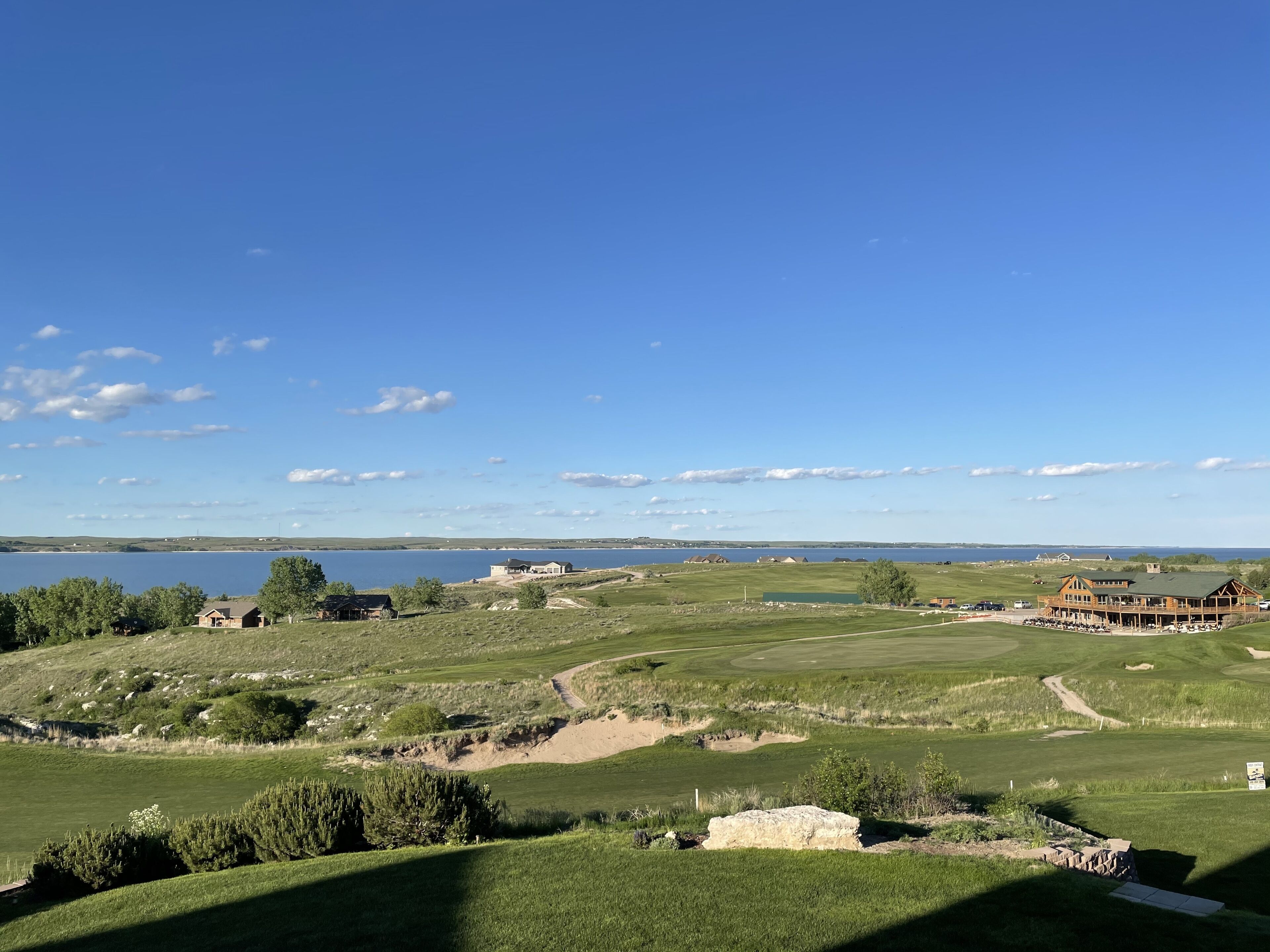 A golf course with a clubhouse, a large body of water, and distant hills.