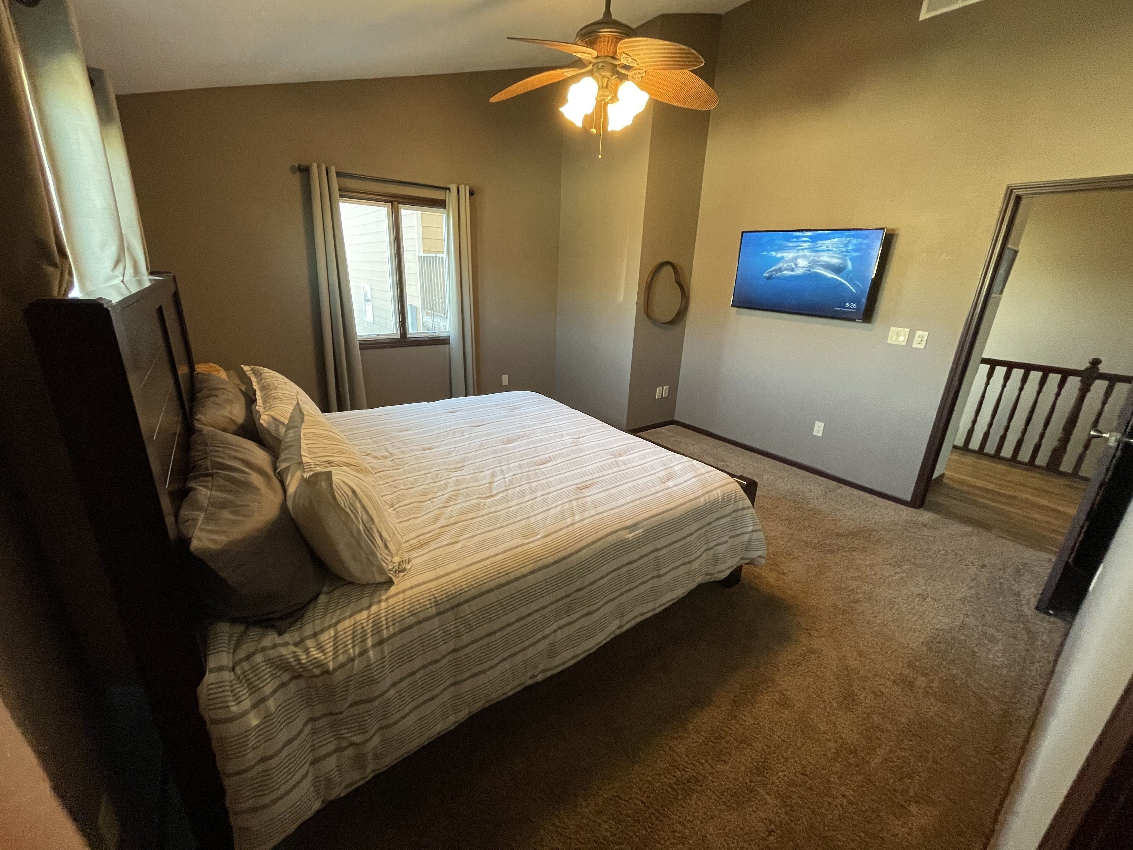 Una camera da letto con un letto, una ventola a soffitto, una TV e una finestra con tende.