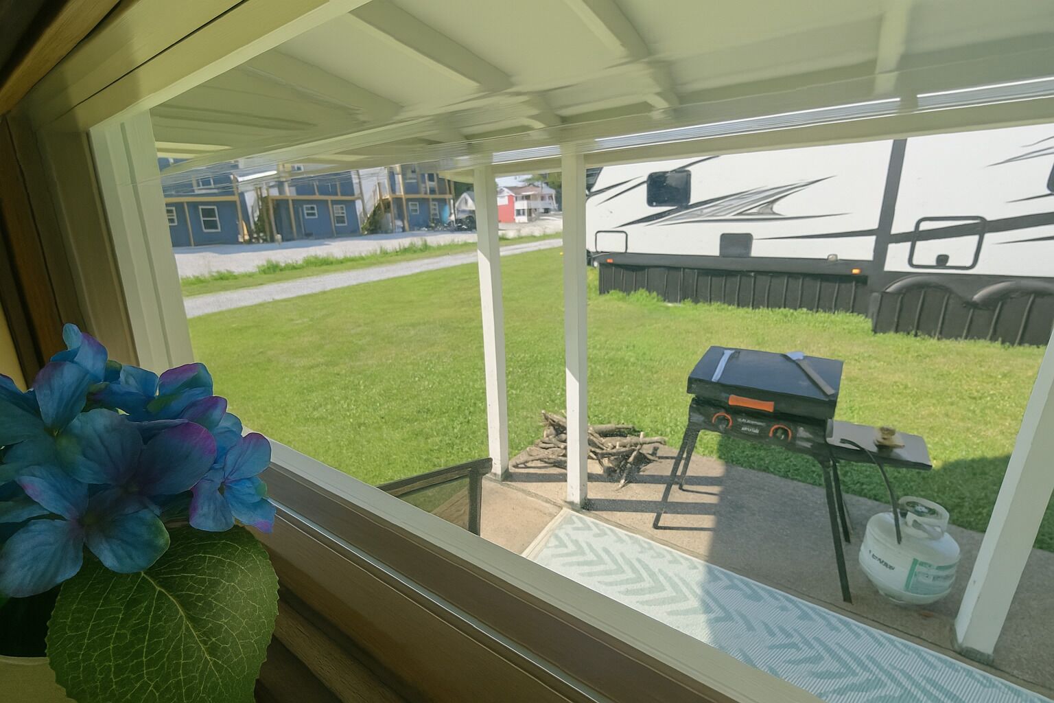 A view through a window of a covered patio area with a grill and a water container.