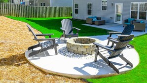A circular patio with Adirondack chairs, a stone fire pit, and a lawn. - Pinehurst Golf Retreat, Pool Table, Fire Pit! (Pinehurst)