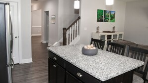 A kitchen with granite countertops, a dining area with chairs, and a staircase leading to another level. - Pinehurst Golf Retreat, Pool Table, Fire Pit! (Pinehurst)