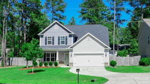 A two-story house with a garage, surrounded by a wooden fence, and a well-maintained lawn. - Pinehurst Golf Retreat, Pool Table, Fire Pit! (Pinehurst)