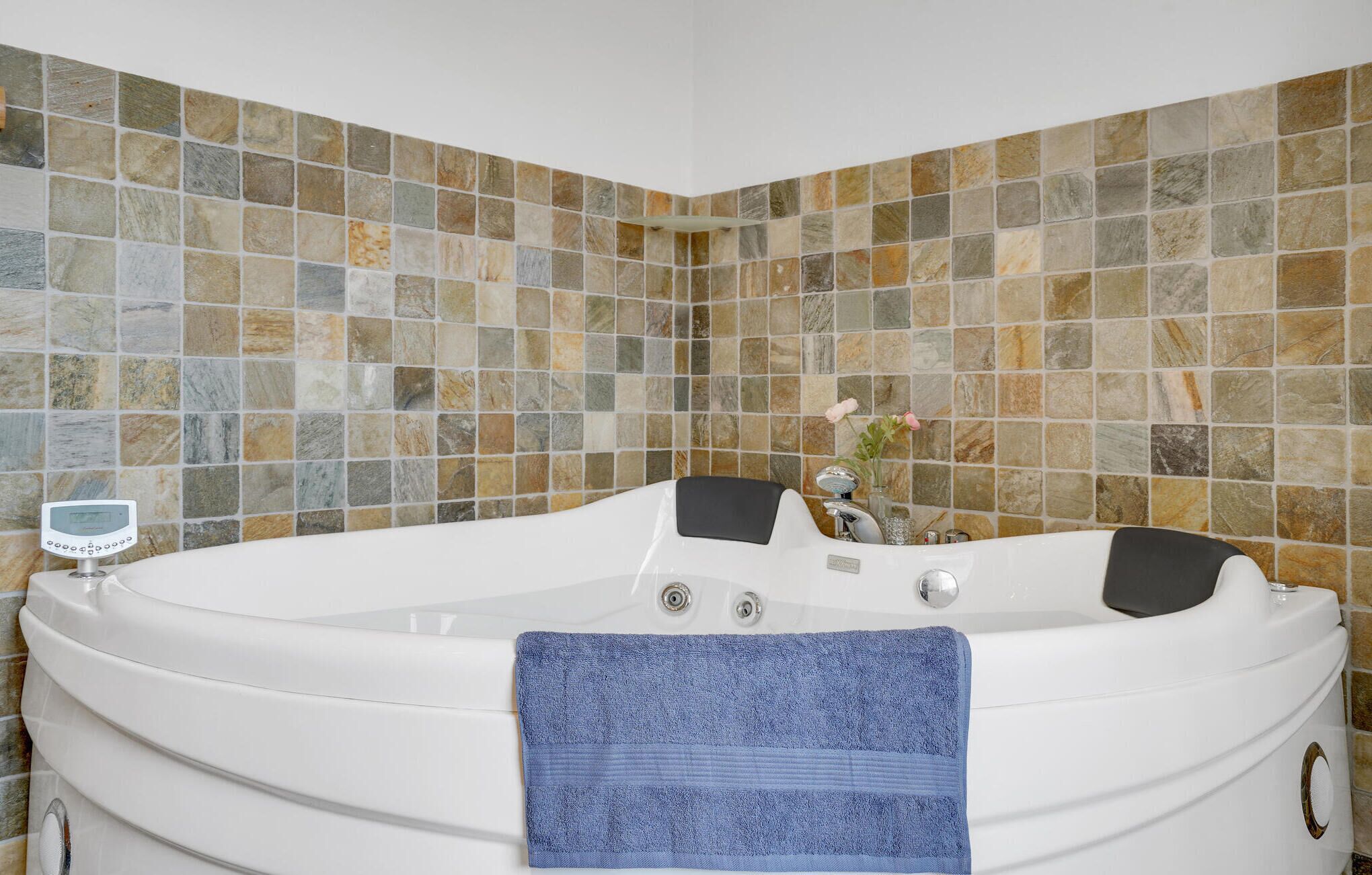 A modern bathroom with a freestanding bathtub, a digital thermometer, and a vase with flowers on the wall.