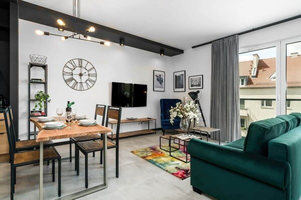 Una sala de estar moderna con comedor, un reloj de pared grande y un televisor de pantalla plana.