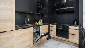 A modern kitchen with black appliances, wooden cabinets, and a stainless steel sink. - Stylish Apartment | Parking and Close to the Old Town (Poznań)