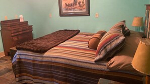 Ein Schlafzimmer mit einem Bett, einer Kommode, einem gerahmten Bild an der Wand und einer Lampe auf dem Nachttisch.