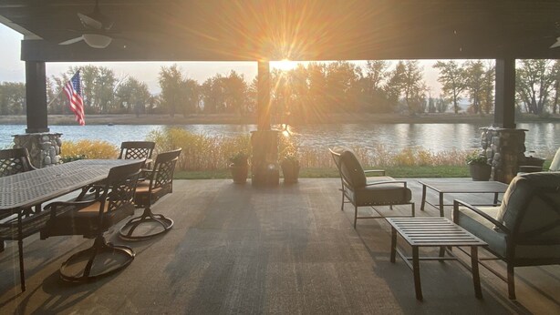 Eine überdachte Terrasse mit Gartenmöbeln, Blick auf einen See und eine amerikanische Flagge.