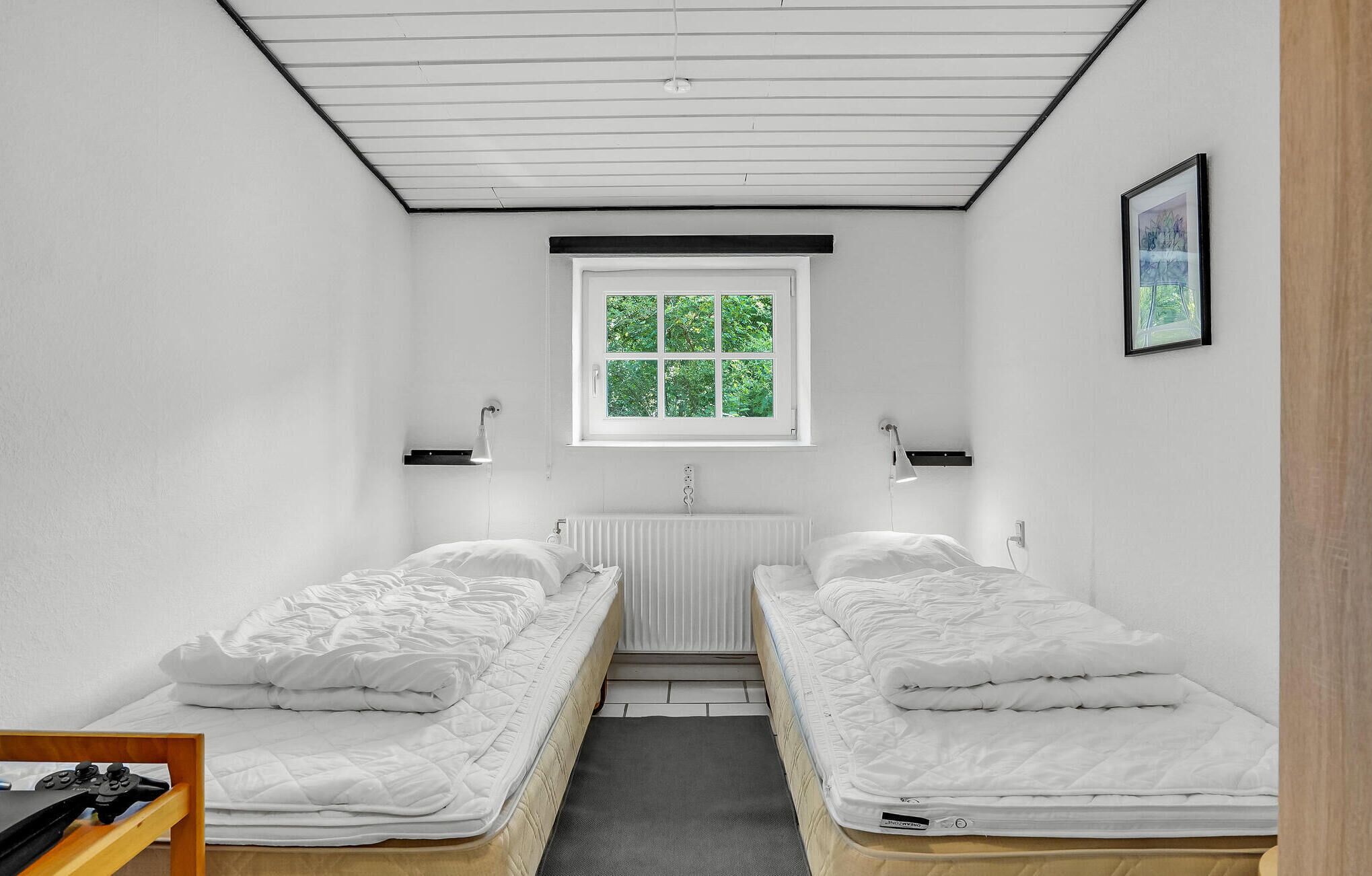 Une petite chambre propre, avec deux lits simples, un radiateur, une fenêtre donnant sur des arbres et un tableau encadré au mur.