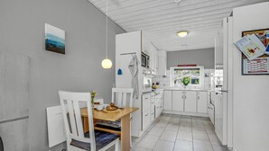 Moderni keittiö, jossa on valkoiset kaapit, ruokapöytä tuoleineen ja riippuvalaisin.