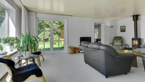 Ein gemütliches Wohnzimmer mit einem grauen Sofa, einem Tisch mit einer Pflanze und einem großen Fenster mit Vorhängen.