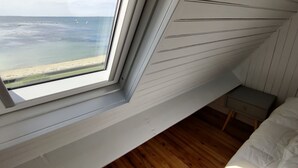 A bedroom with a large window overlooking a beach, a wooden floor, and a small bedside table. - Magnificent sea view, direct access to the beach. 4-person apartment (Damgan)