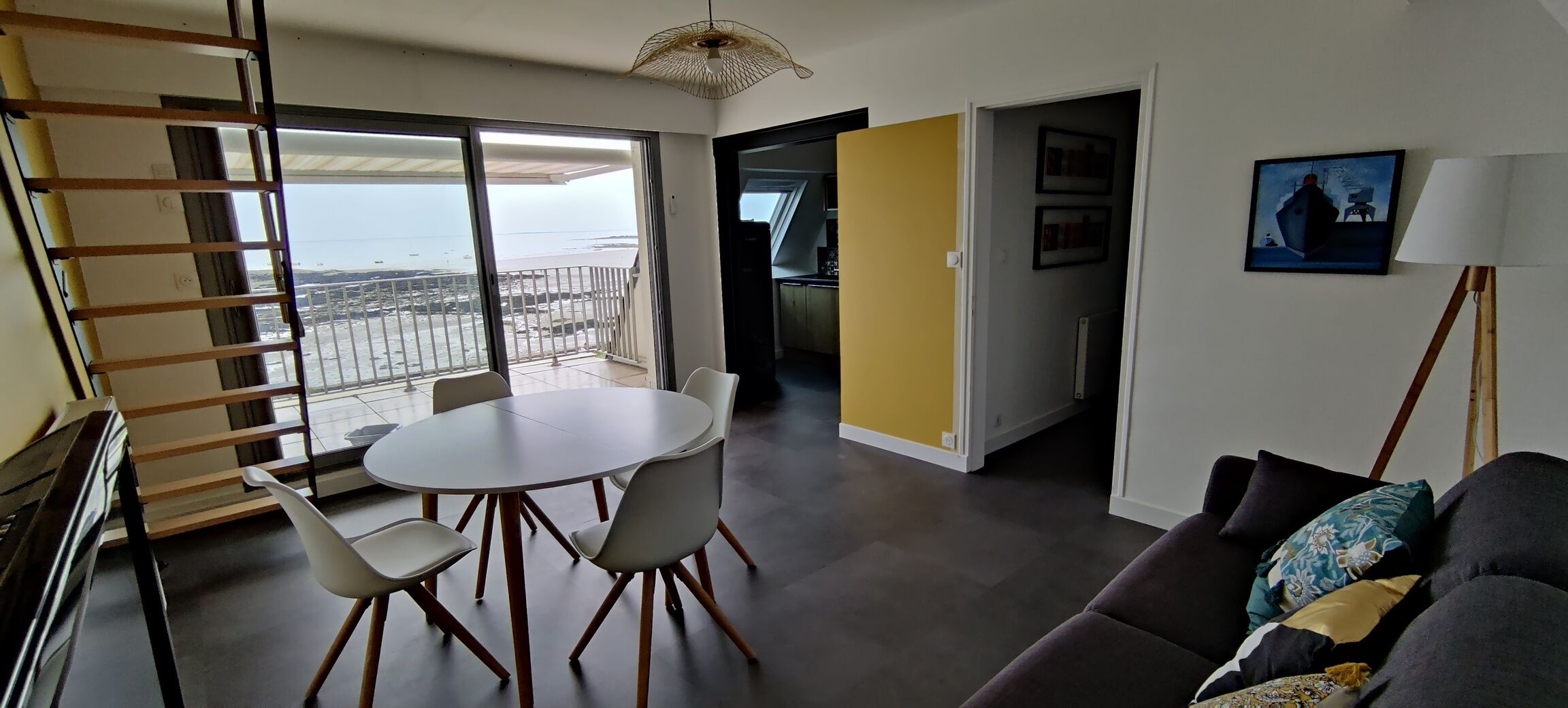 A modern living room with a balcony, a dining area, and a view of the sea.