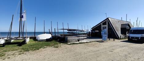 A beachside building with a sloped roof, a covered area for boats, and a parked van.