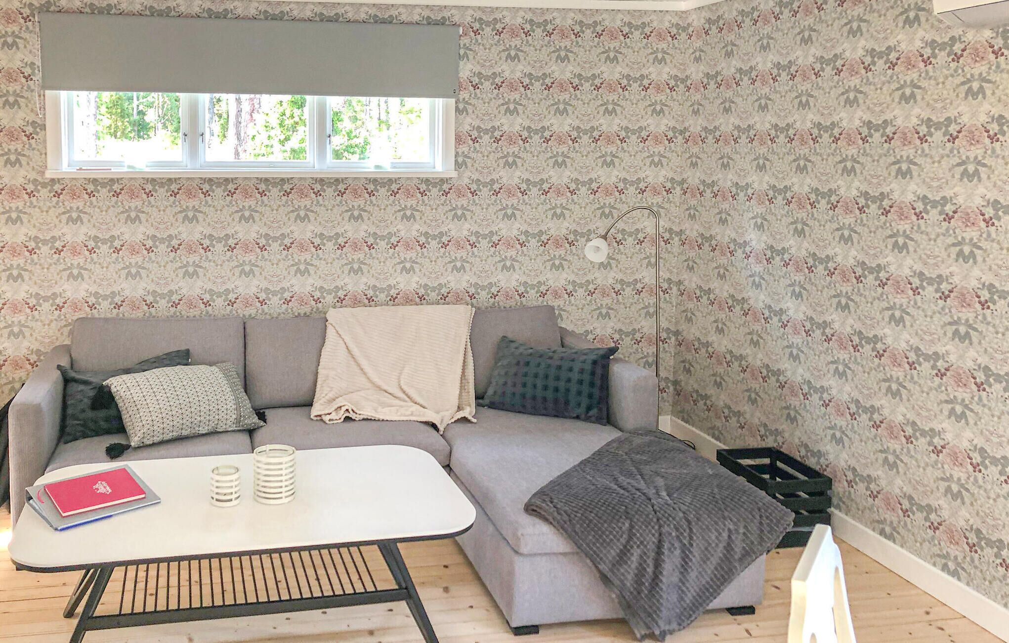 A cozy living room with a grey sofa, a white coffee table, and a floral-patterned wallpaper.