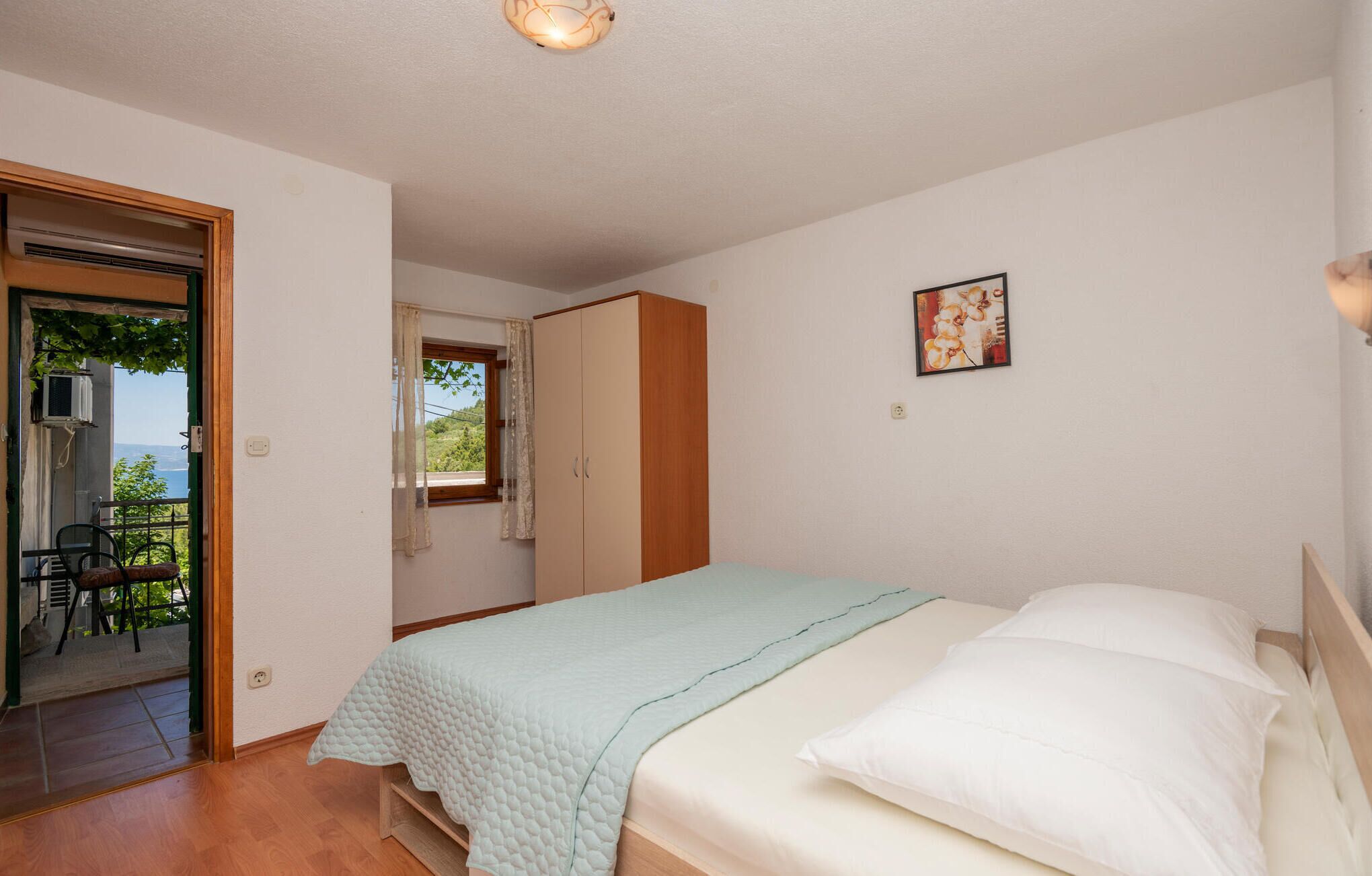 A bedroom with a bed, a wardrobe, a door leading to an outdoor area, and a small window with curtains.