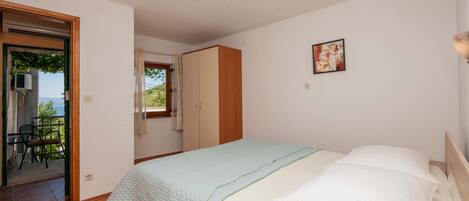 A bedroom with a bed, a wardrobe, a door leading to an outdoor area, and a small window with curtains.