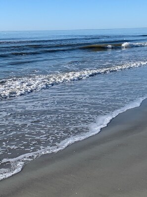 A beach with waves gently lapping onto the shore. - Beautiful, Clean, Pool off back deck, Ocean/Beach across street, Desirable area. (Hilton Head Island)