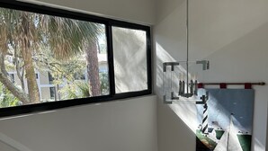 Ein modernes Interieur mit weißer Geländer, einem großen Fenster mit Blick auf Palmen und Gebäude, und einem Segelboot-Gemälde an der Wand.