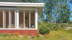 Une maison de plain-pied avec un porche abrité, un petit jardin où poussent différentes sortes de fleurs, et un ciel bleu clair en arrière-plan.