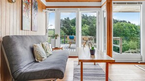 Un salon moderne avec un canapé gris, un plafond en bois et de grandes fenêtres donnant sur un paysage verdoyant.