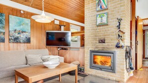 Un salon chaleureux avec une cheminée, des murs en bois, un téléviseur à écran plat et des œuvres d’art.