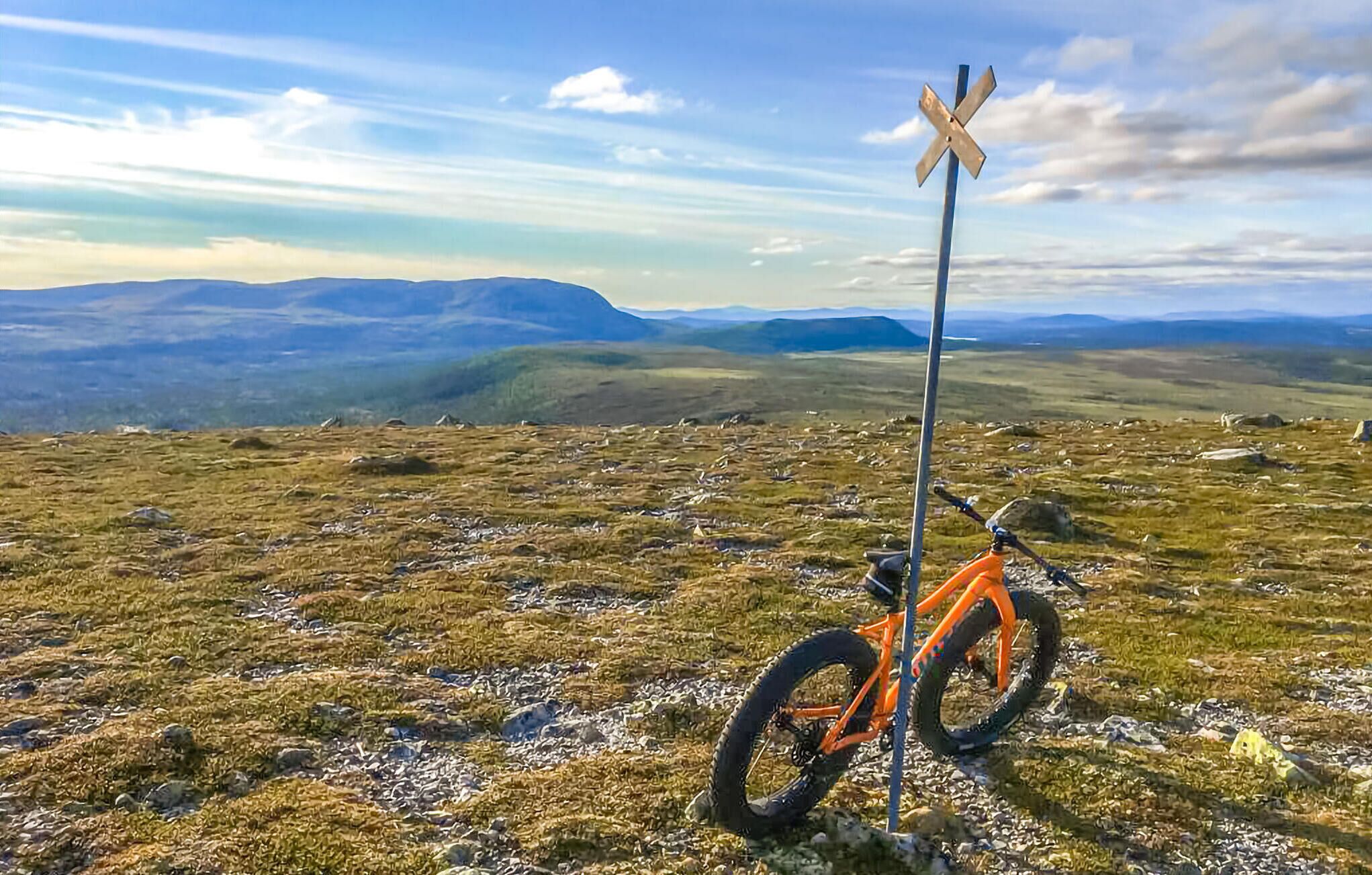Una bicicleta de montaña aparcada en un campo cubierto de hierba, con una señal de paso a nivel en el fondo.