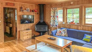 Un intérieur de chalet chaleureux avec un téléviseur, des meubles en bois, une cheminée et de grandes fenêtres.