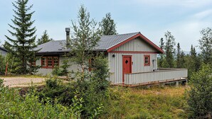 Une cabane en bois avec une porte rouge et un petit porche, entourée d’une forêt dense.