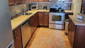 A kitchen with wooden cabinets, a stainless steel refrigerator, a microwave, an oven, and a coffee maker. - Pompano Holiday Gem (Pompano Beach)