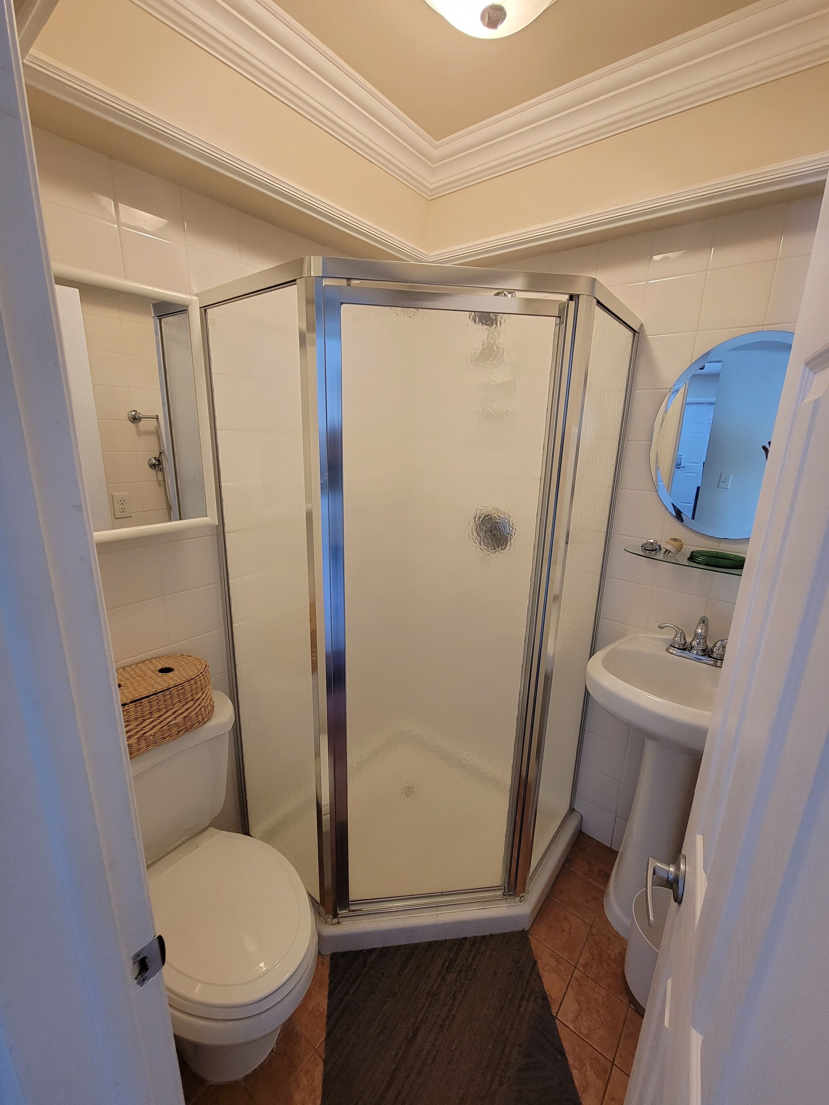 Un bagno moderno con doccia vetro, water, lavandino e specchio.