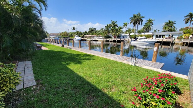 A marina with boats docked, a grassy area with red flowers, and palm trees. - Pompano Holiday Gem (Pompano Beach)