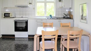 Cucina con mobili bianchi, piano cottura, forno a microonde, lavello e una finestra vista verde. Due sedie di legno attorno a un tavolo.