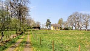 Een landelijk landschap met een onverharde weg, een geel huis en een omheind veld.