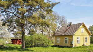 Een geel huis met een schuin dak, omringd door een grasveld en bomen.