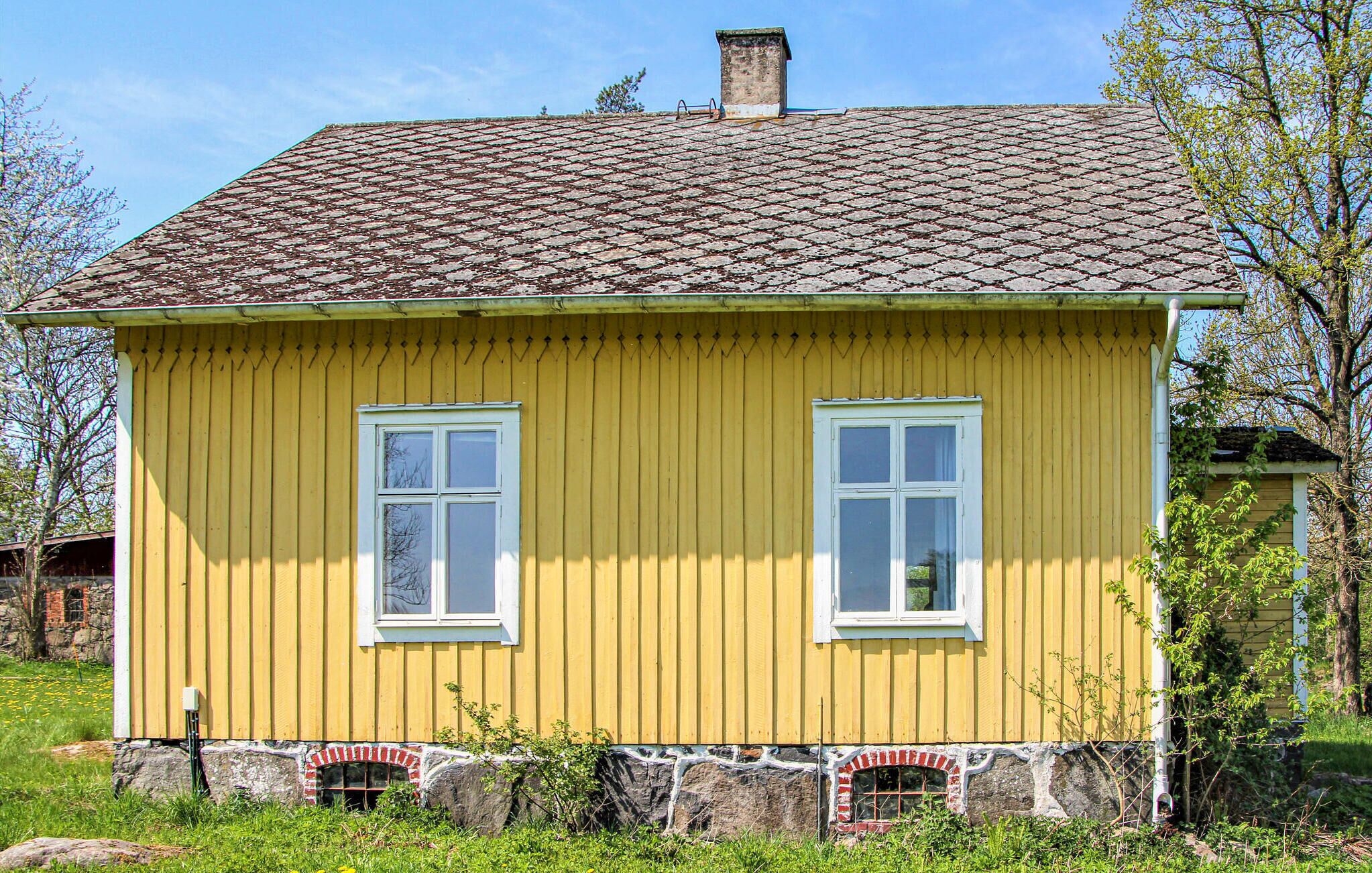 A yellow wooden house with two windows and a tiled roof.