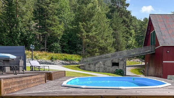 En træterrasse med et boblebad, et spiseområde med stole, og en rød bygning med et skråt tag.
