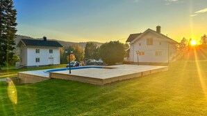 Et hus med swimmingpool, græsplæne og solnedgang i baggrunden.
